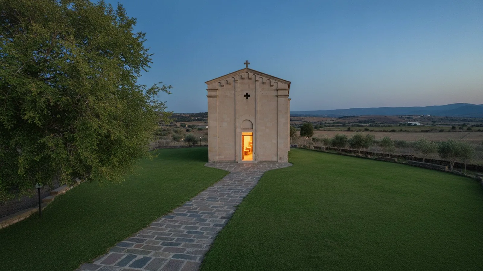 Una chiesa campestre in pietra al tramonto, circondata dal prato